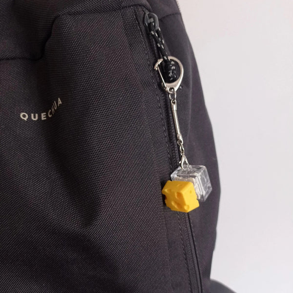 Llavero original con diseño de cubo transparente y pieza amarilla de queso colgando en mochila negra Quechua