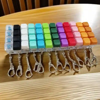Llaveros originales con teclas de colores variados y gancho de metal en fila sobre una mesa de madera