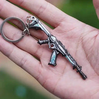Llavero gamer metálico con forma de rifle futurista, ideal para fans de videojuegos.