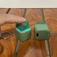 Green frog pop-up keychain with LED light on wooden surface, USB charging port visible