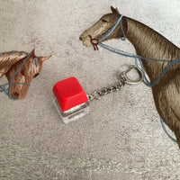 Llavero creativo con botón rojo y base transparente sobre tela bordada con caballos
