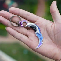 Llavero gamer de metal en forma de cuchillo curvo con acabado iridiscente, ideal para fans de videojuegos.