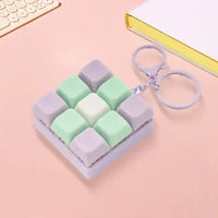 Llavero creativo con diseño de teclas de teclado en colores pastel verde, lila y blanco sobre fondo rosa
